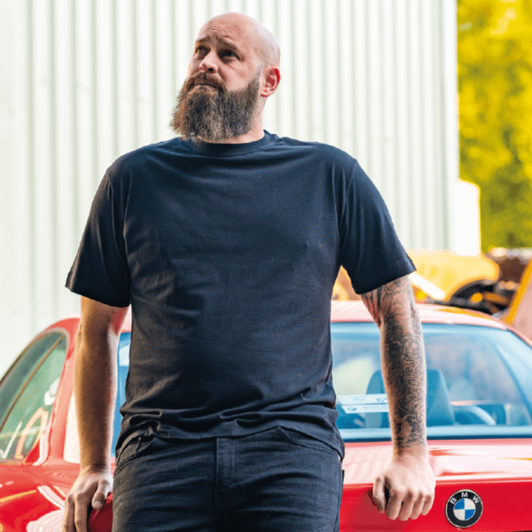 Model sporting the Plain Tee in Black from On the Spanners while leaning on his BMW